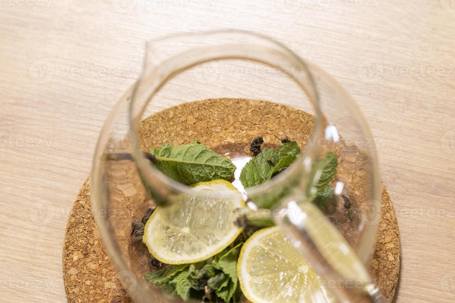 Stylish transparent tea pot with dried tea leaves, mint leaves and lemon slices in it. Beverage photo