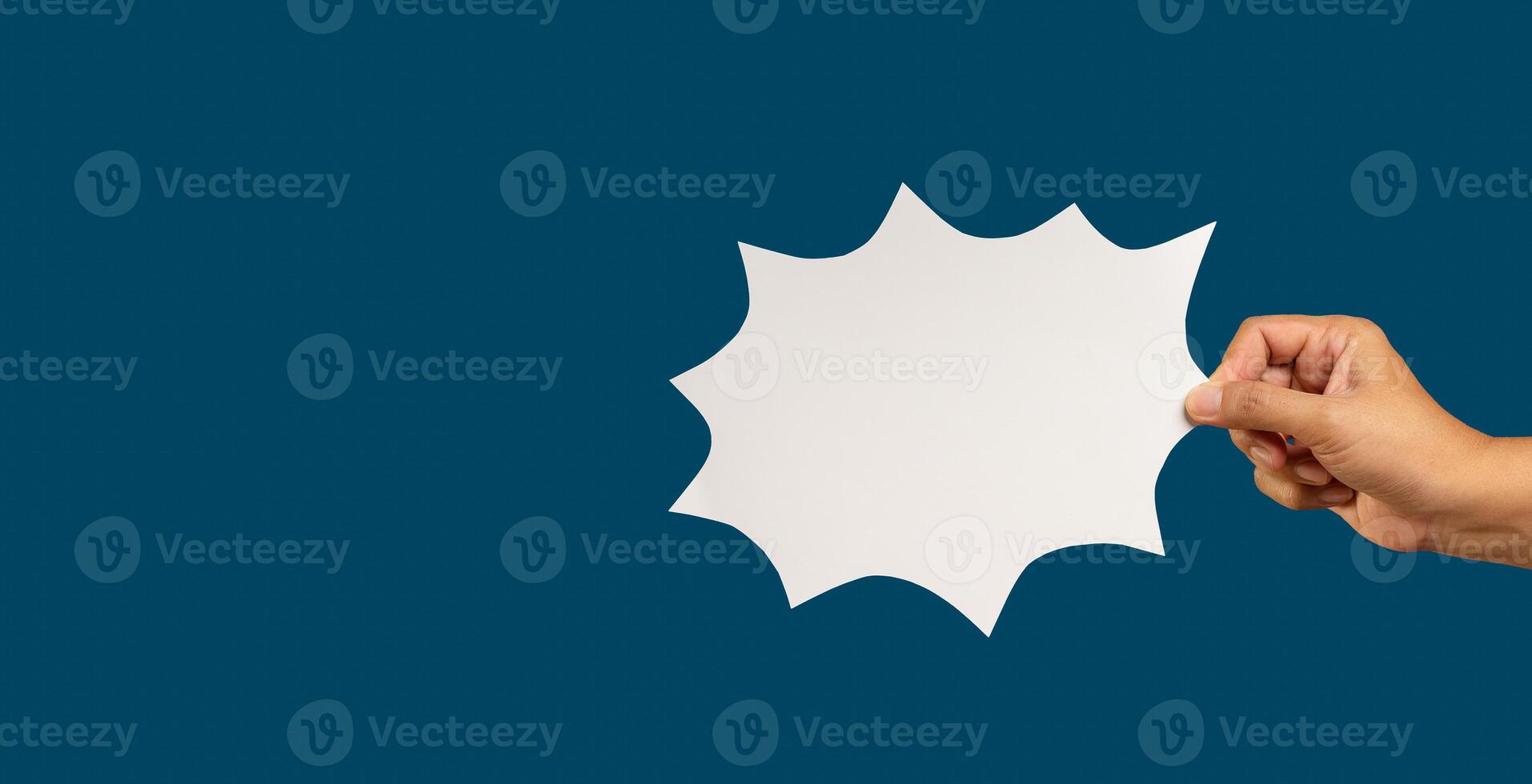 Hand holding a blank white comic speech bubble while standing against a blue background. photo