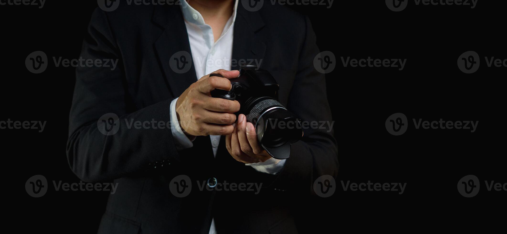 Close-up of a photographer in a suit holding the digital camera while standing on a black background photo