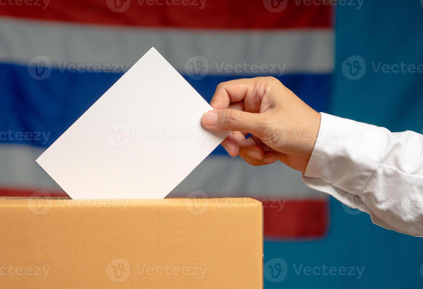 Hand voter holding ballot paper putting into the voting box at place election against the Thailand flag background photo