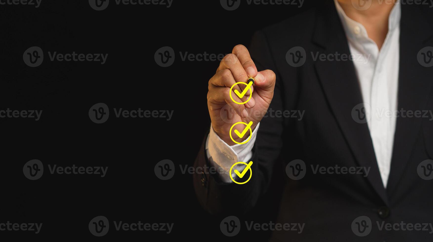 Businessman holding a pen and checking a mark on the boxes symbol is one of three options while standing on a black background. Space for text. photo