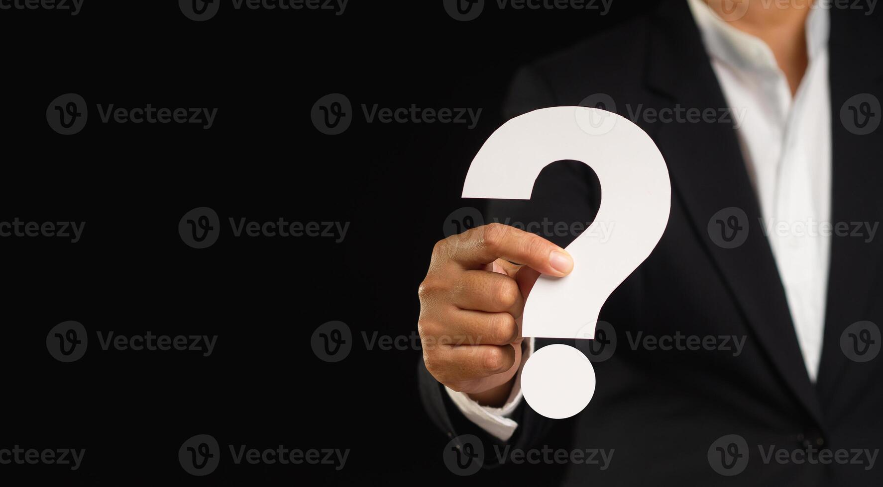 Close-up of a businessman holding a white question mark symbol while standing against a black background photo