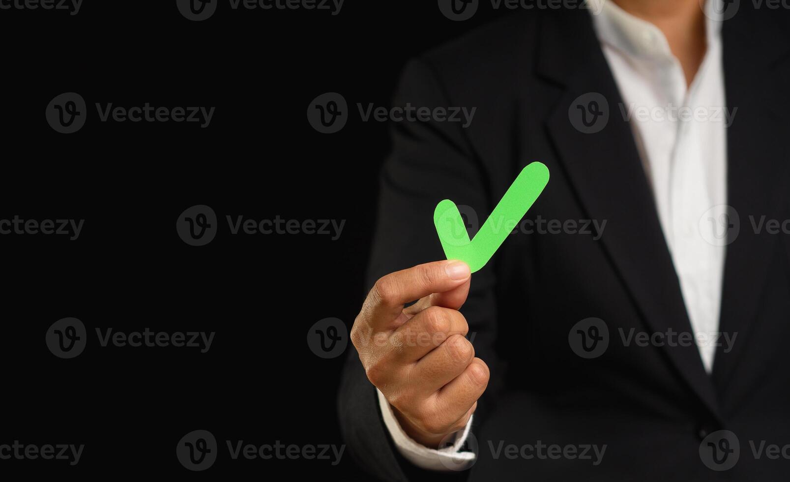 Businessman in a suit holding a green check mark symbol while standing on a black background photo