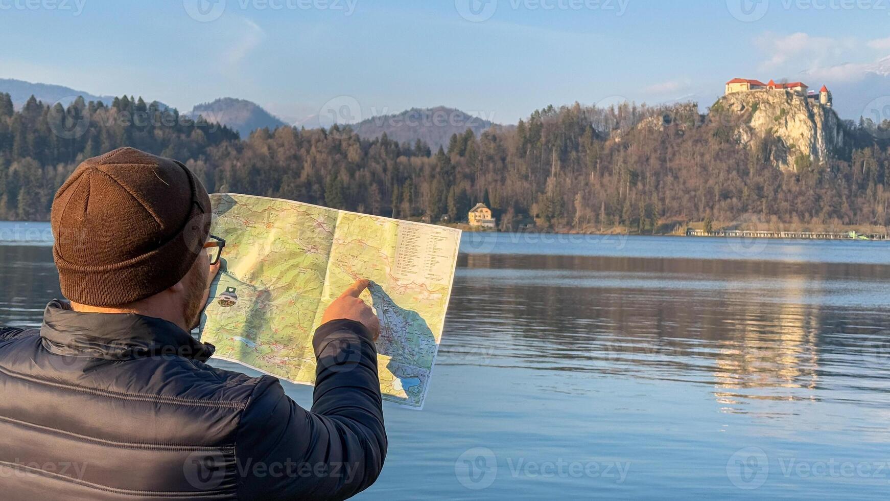 A contemplative Asian man with a map beside tranquil lakeside scenery, embracing Wanderlust Day and Cartography Week explorations photo