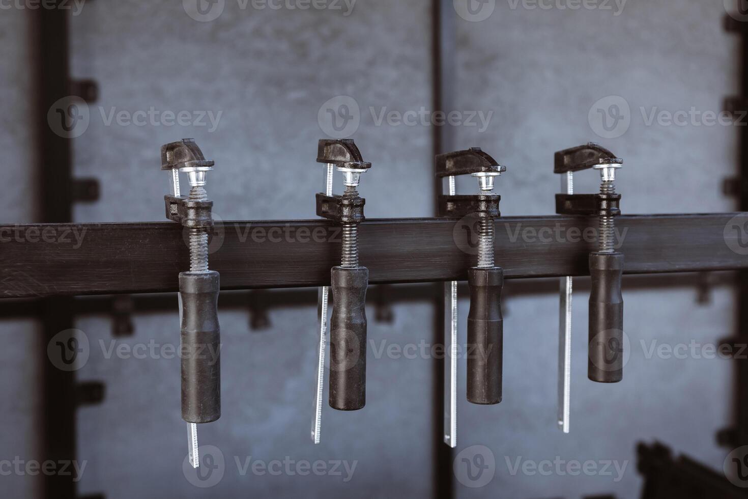 Four black clamps hang on a metal stand against a background of a slate wall on the construction site, prepared for fixing materials photo