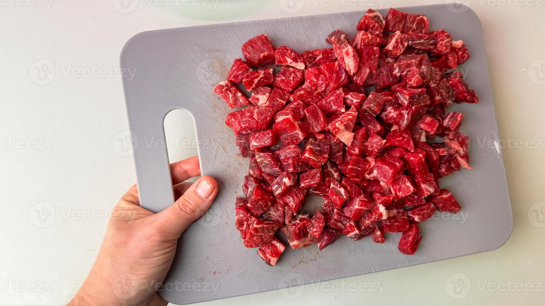 Hand gripping cutting board adorned with vibrant diced beef, ready for carnivorous feasts, reminiscent of South American asados photo