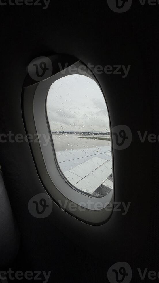 Glimpsing through a rain kissed airplane porthole, the wing whispers tales of untold journeys on Jet Lag Awareness Day photo