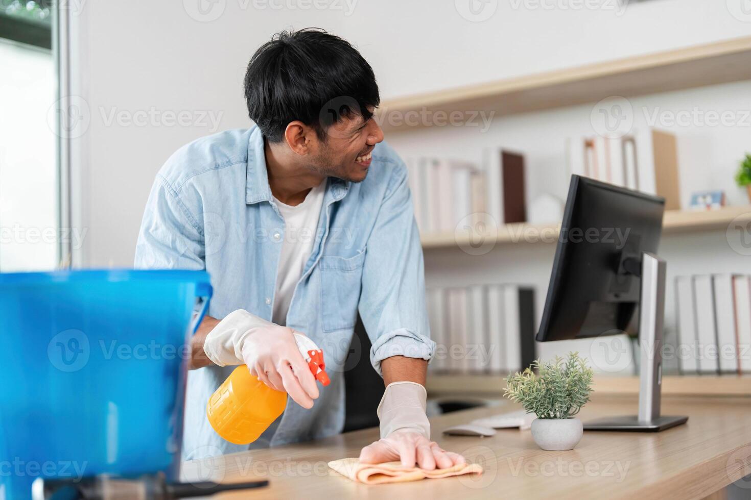 Office Cleaning and Maintenance. Young man using spray cleaner and cloth to tidy workspace. photo