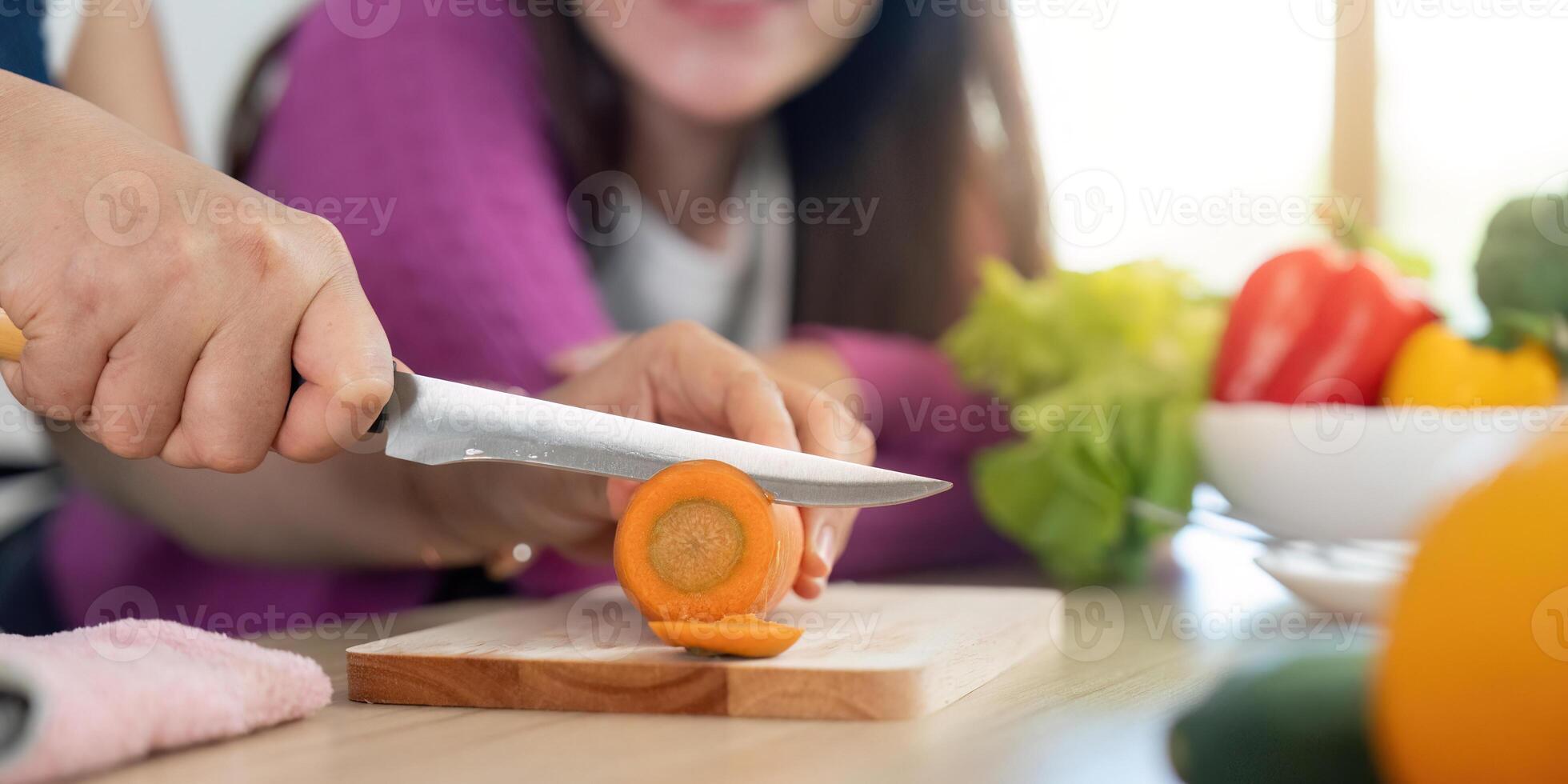 Chopping Fresh Vegetables. Close-up of a woman slicing a carrot while another woman observes. photo