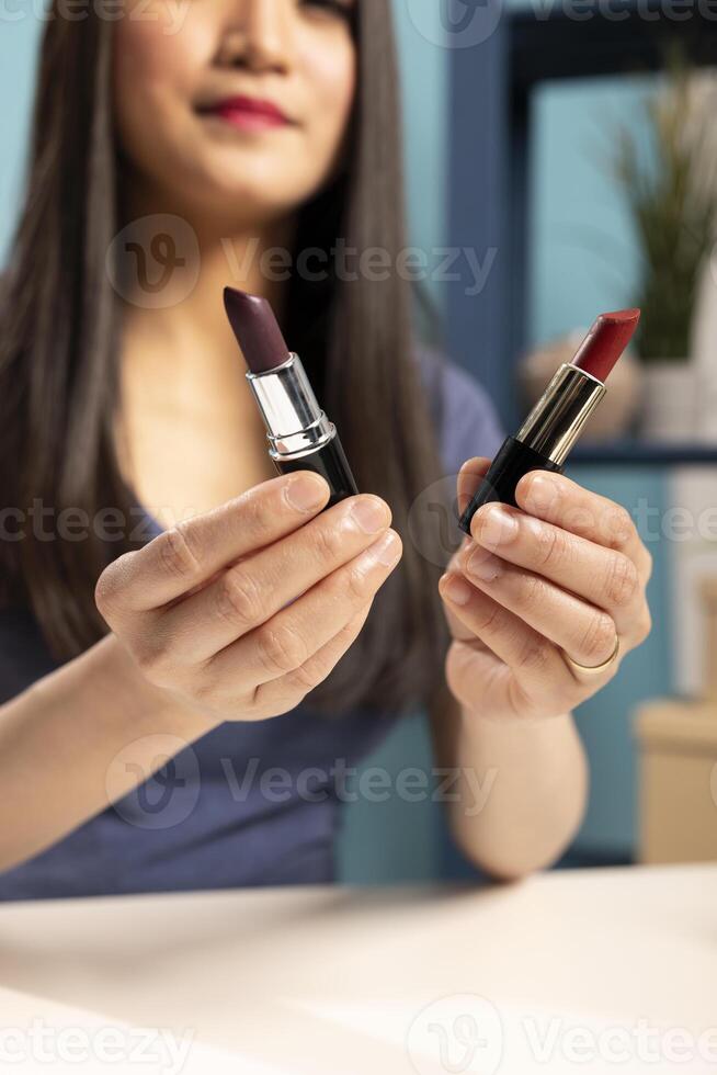 Selective focus on various lipstick shades held by a beautiful woman, showcasing them to the camera during her vlogging session. Closeup of makeup products presented by an asian beauty blogger. photo