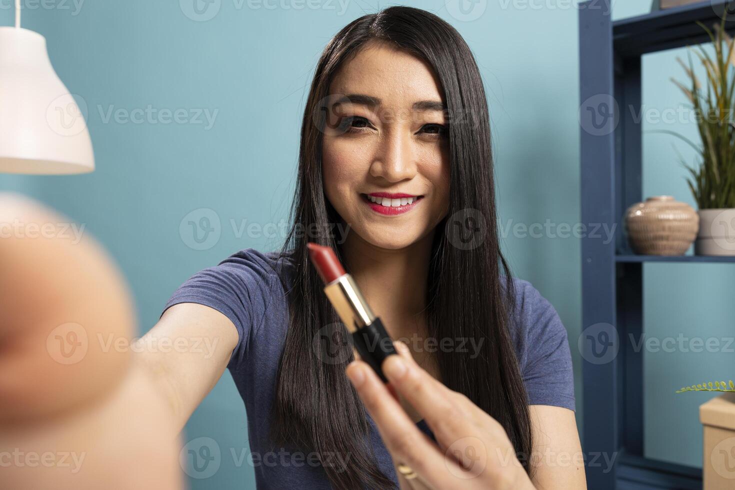 Asian makeup artist holds the camera, offering expert advice on makeup tips and product demonstrations, engaging her online audience. POV of cheerful beauty influencer sharing latest lipstick shade. photo