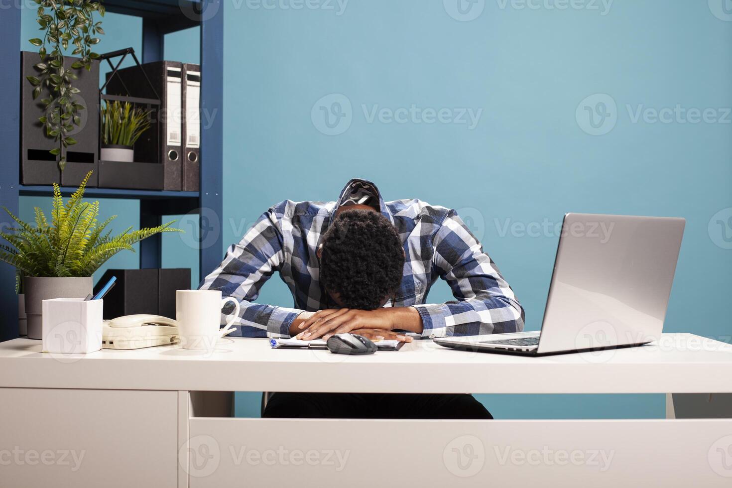 Overworked male entrepreneur collapsed on his office desk from fatigue after long work hours, showing stress and burnout. Exhausted businessman resting head on table from tiredness. photo