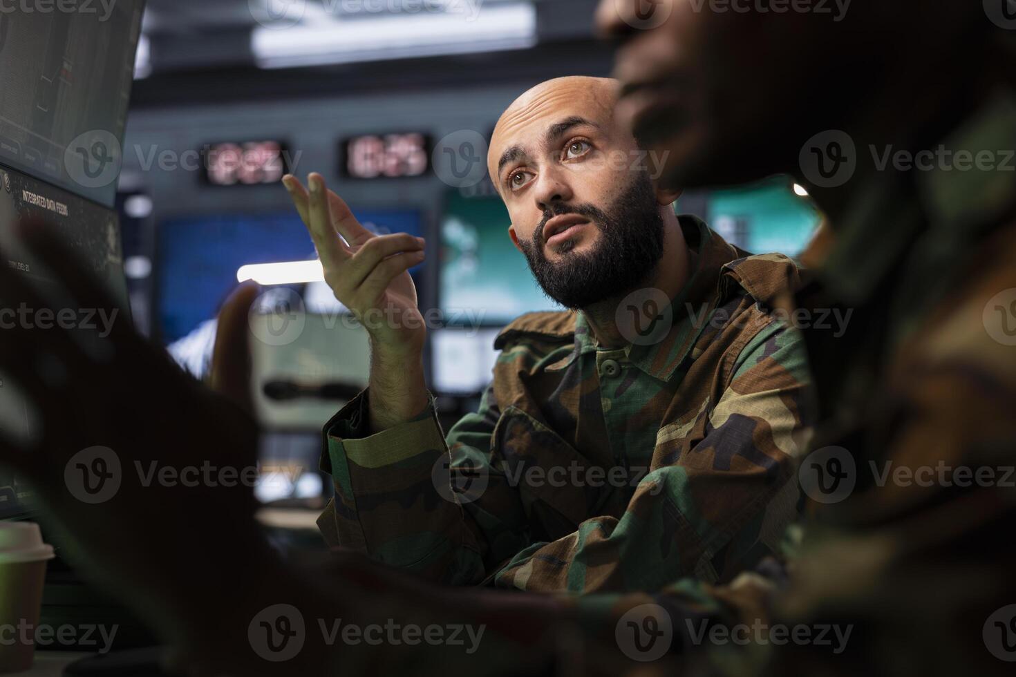 Military agent and colleague in command post doing reconnaissance mission using monitoring equipment. Middle Eastern army expert uses maps and charts to determine location of targets photo
