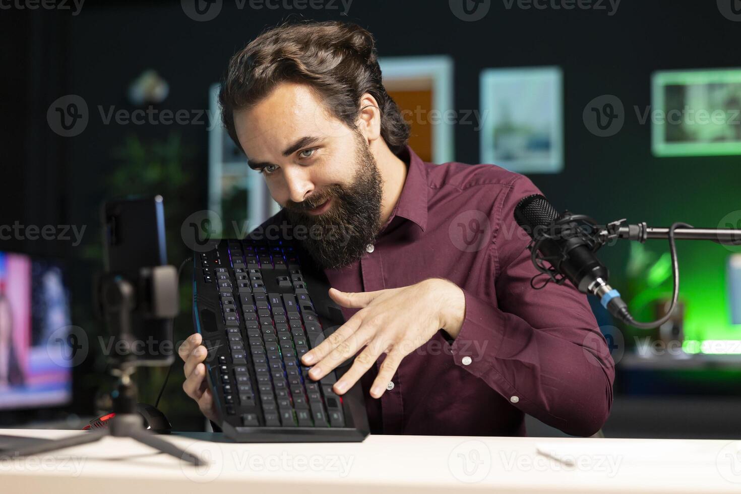 Tech guru promoting mechanical keyboard from sponsor to subscribers. Content creator paid by brand to showcase computer peripheral device with neon lit keys in home studio photo