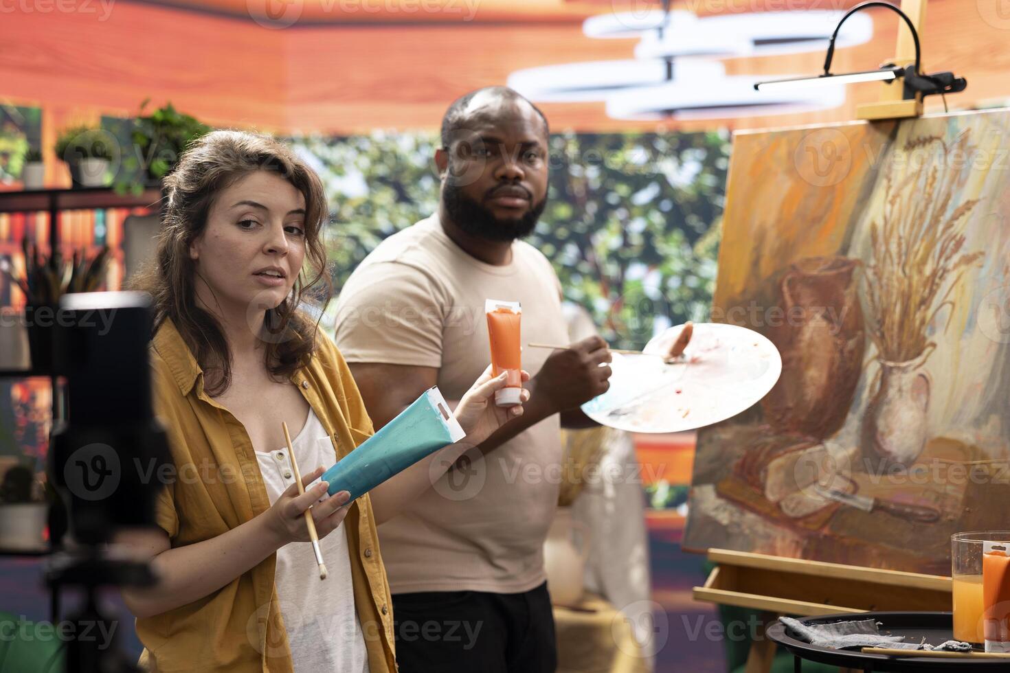 Woman artist hosting an online class to present products and technique used on a rustic artwork, recording a tutorial online. Team of painters doing a master class for e learning, art instruction. photo