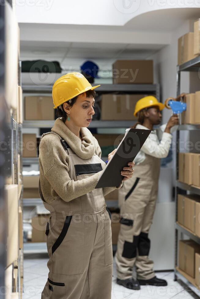 Woman warehouse worker ensures inventory management with boxes on racks, focusing on goods dispatch and quality control operations. Pallets stacked in the industrial storehouse. photo