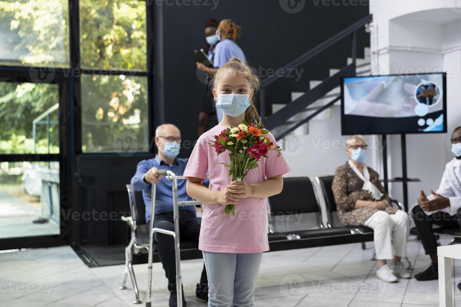 Young kid visiting elderly grandparent in medical facility waiting area, holding flowers bouquet to show love and support while wearing mask and following healthcare protection rules. photo