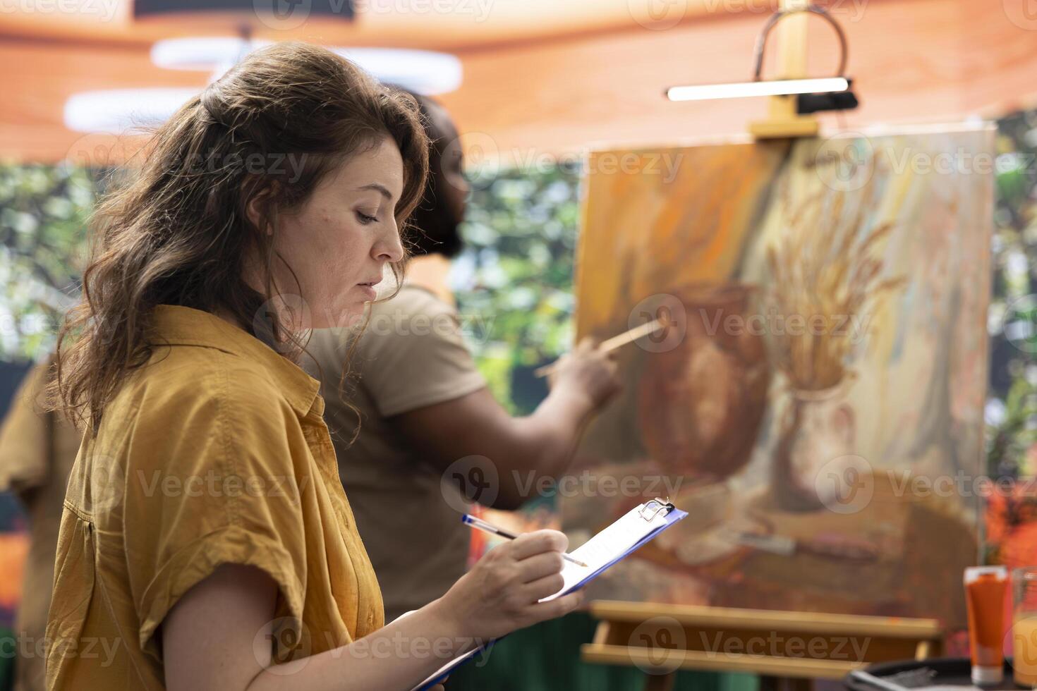 Skilled master painter keeps account of her apprentice techniques, following his creative process and teaching him new ideas. Beginner artist listening to advice from experienced woman. photo