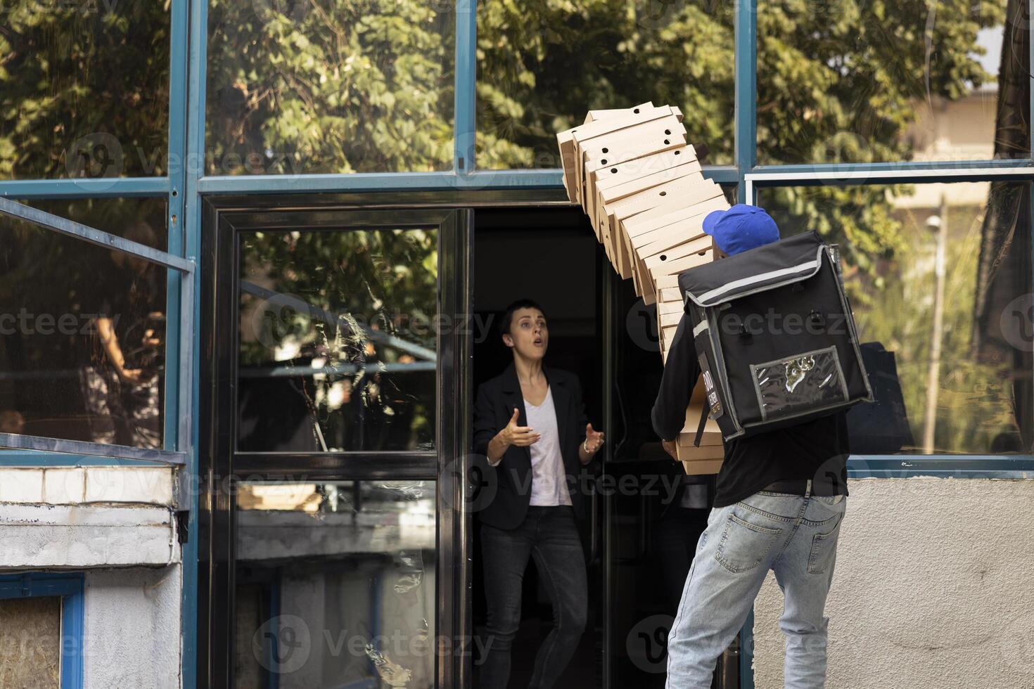 African american worker makes a mistake while he is delivering pizza, stumbling as he trips over and drops the stack of pizza boxes. Confused customer for the poor courier service experience. photo