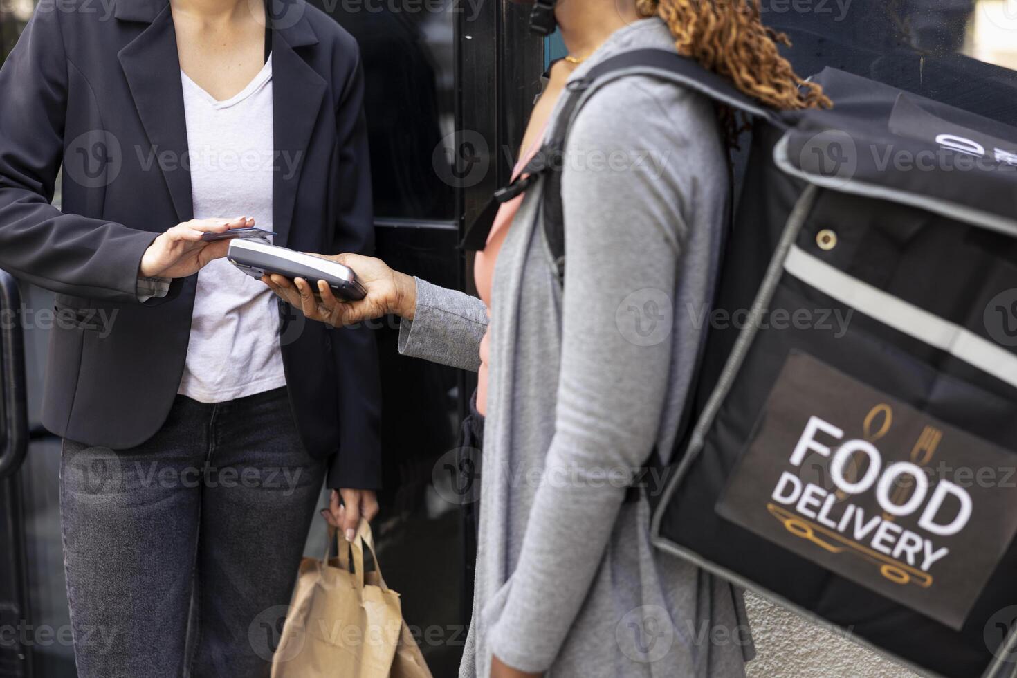 Modern courier has meal order and pos terminal for client to pay, customer taps her card on a wireless device. Employee ensuring quick service and smooth transaction for takeaway system. photo