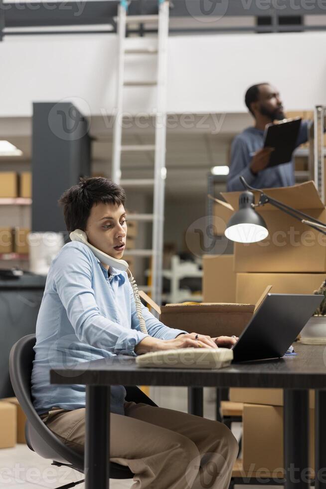 Female staff member overseeing product handling and distribution systems in a fulfillment center, working on hand packing goods surrounded by storage shelves for small scale depot. photo