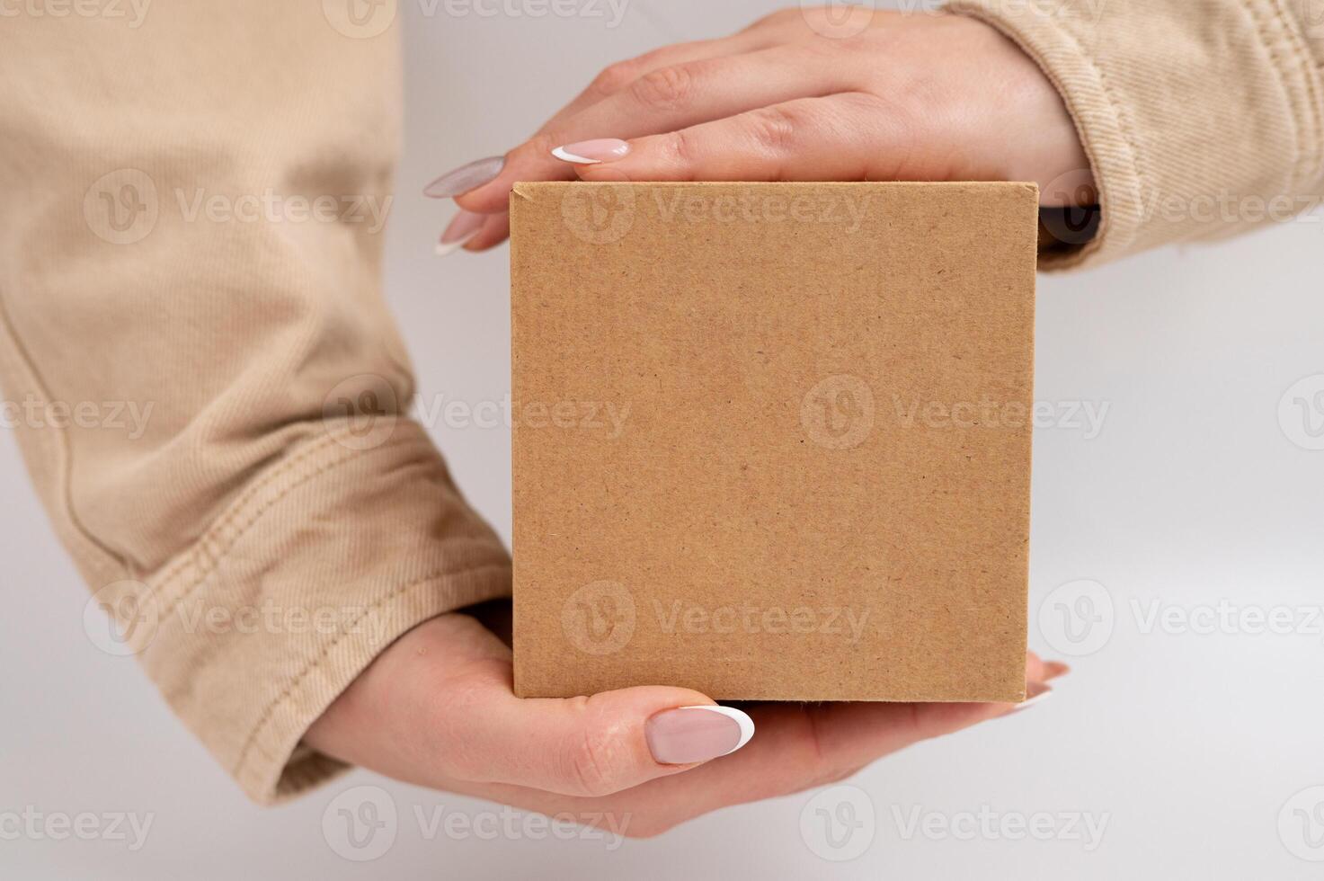 Woman holding plain brown box with hands displaying neutral manicure. National Cartonnage Day photo