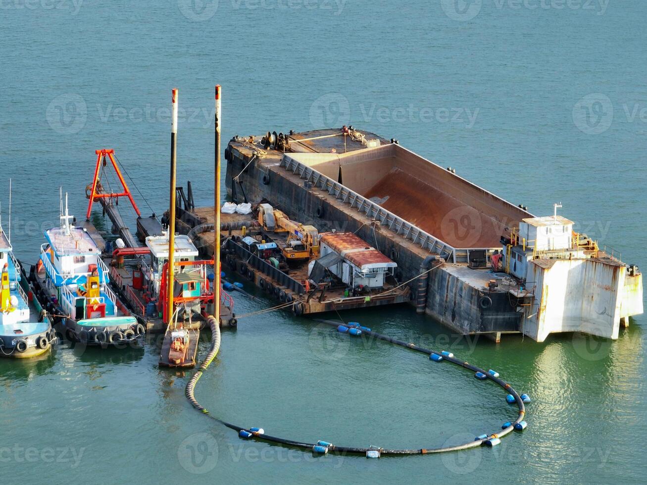Heavy maritime engineering vessel conducting offshore dredging work with crane equipment and support boats in coastal waters for port deepening and marine construction infrastructure development photo