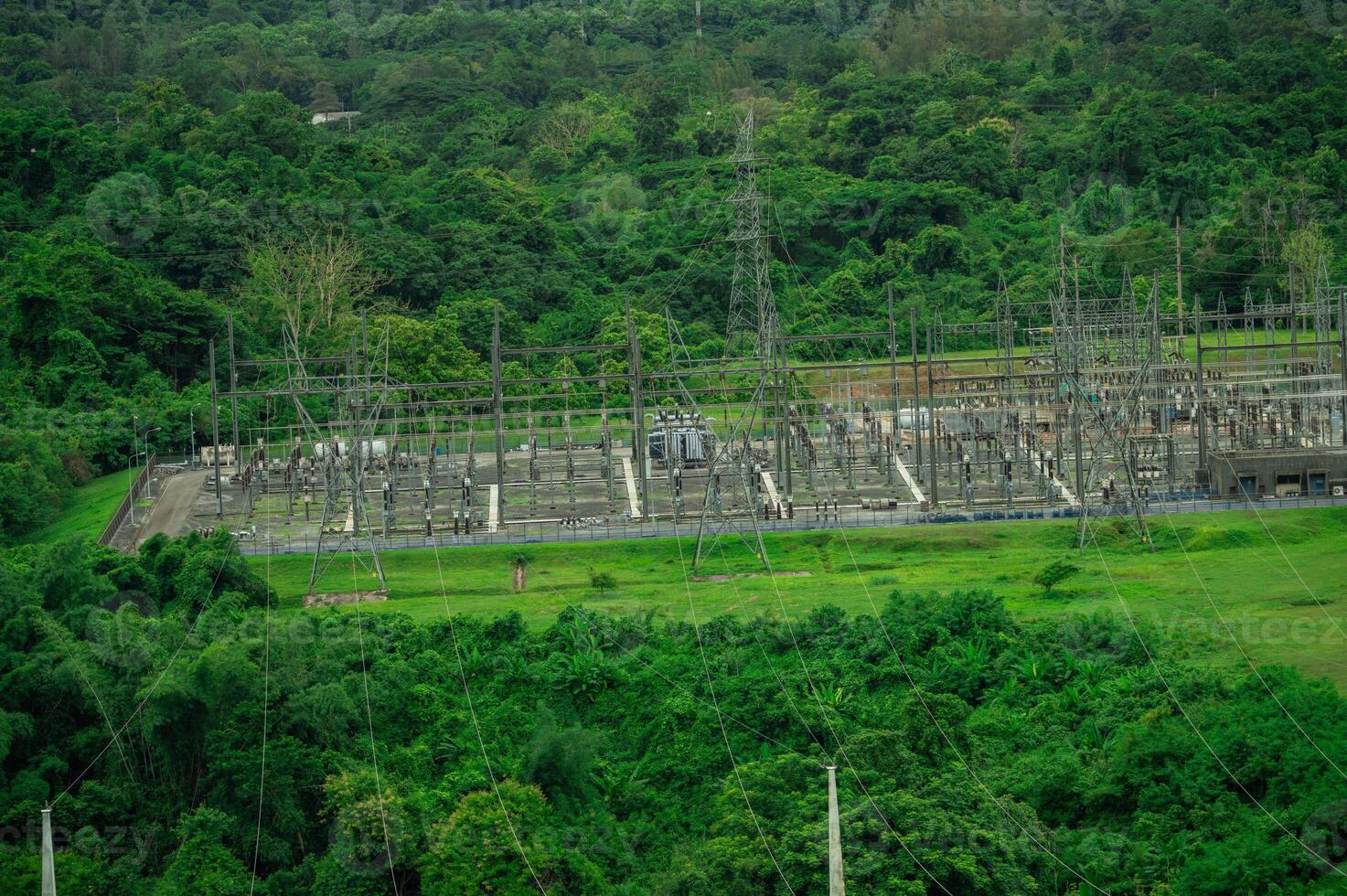 Electrical power station at hydroelectric dam facility with green forest. Sustainable renewable energy infrastructure technology. Power transmission substation near dam. Sustainable power generation photo