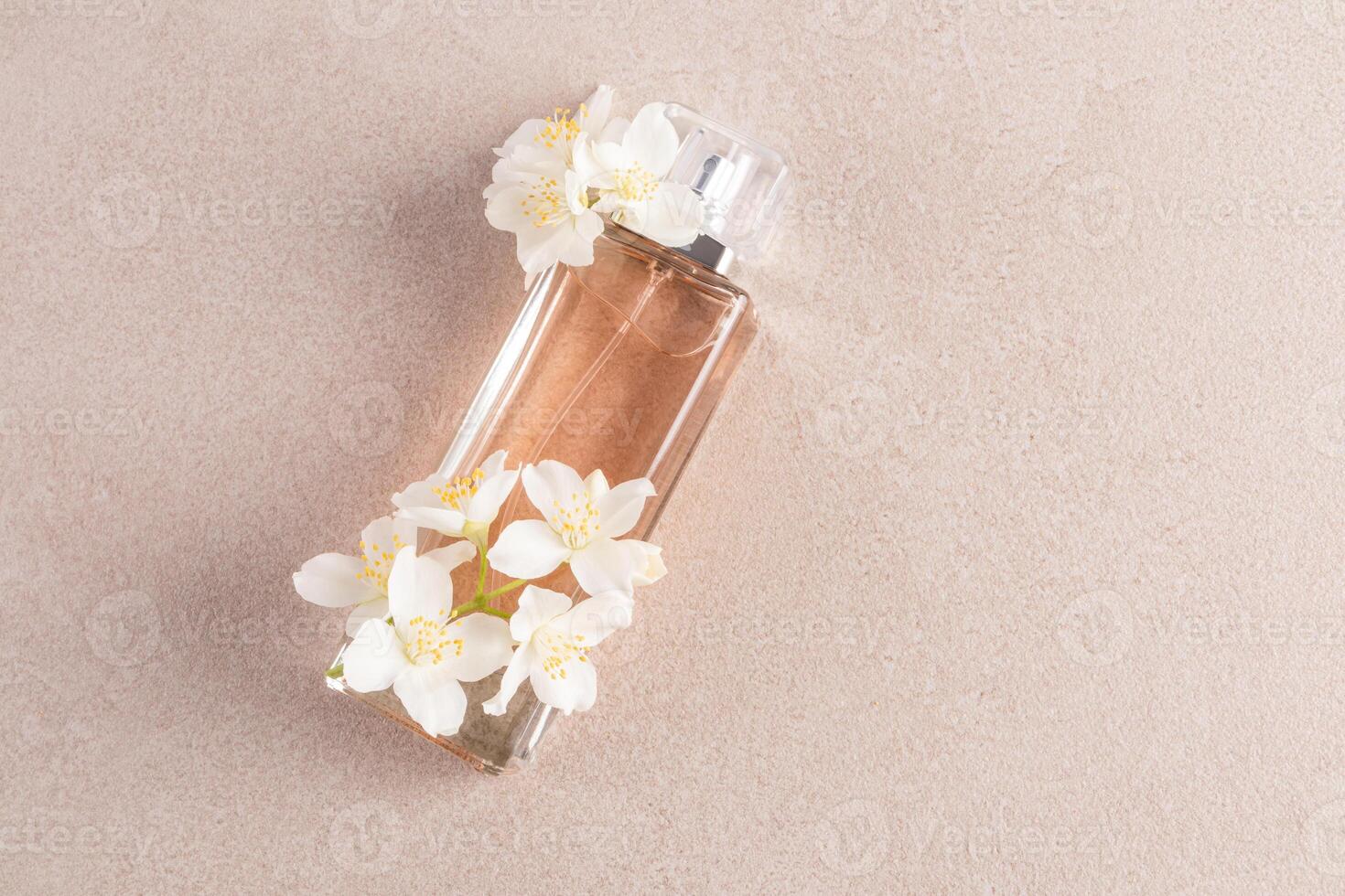 An elegant bottle of cosmetics, cologne, perfume lies on a stone beige background with white jasmine flowers. Upper view. A copy of the space. photo