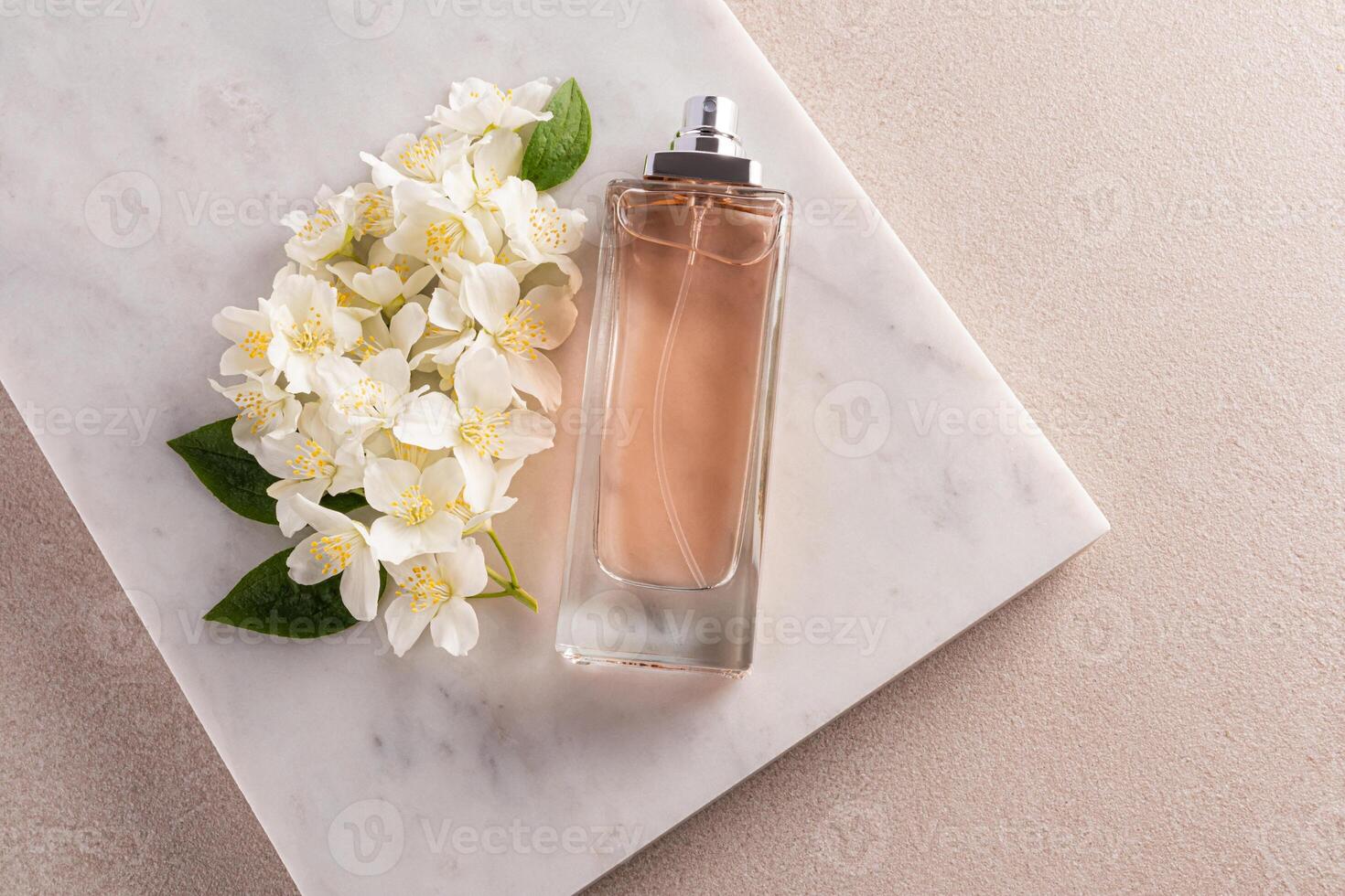 A tall elegant bottle of perfume, cosmetic spray, cologne lies on a piece of marble with numerous white jasmine flowers. top view. blank bottle mockup photo