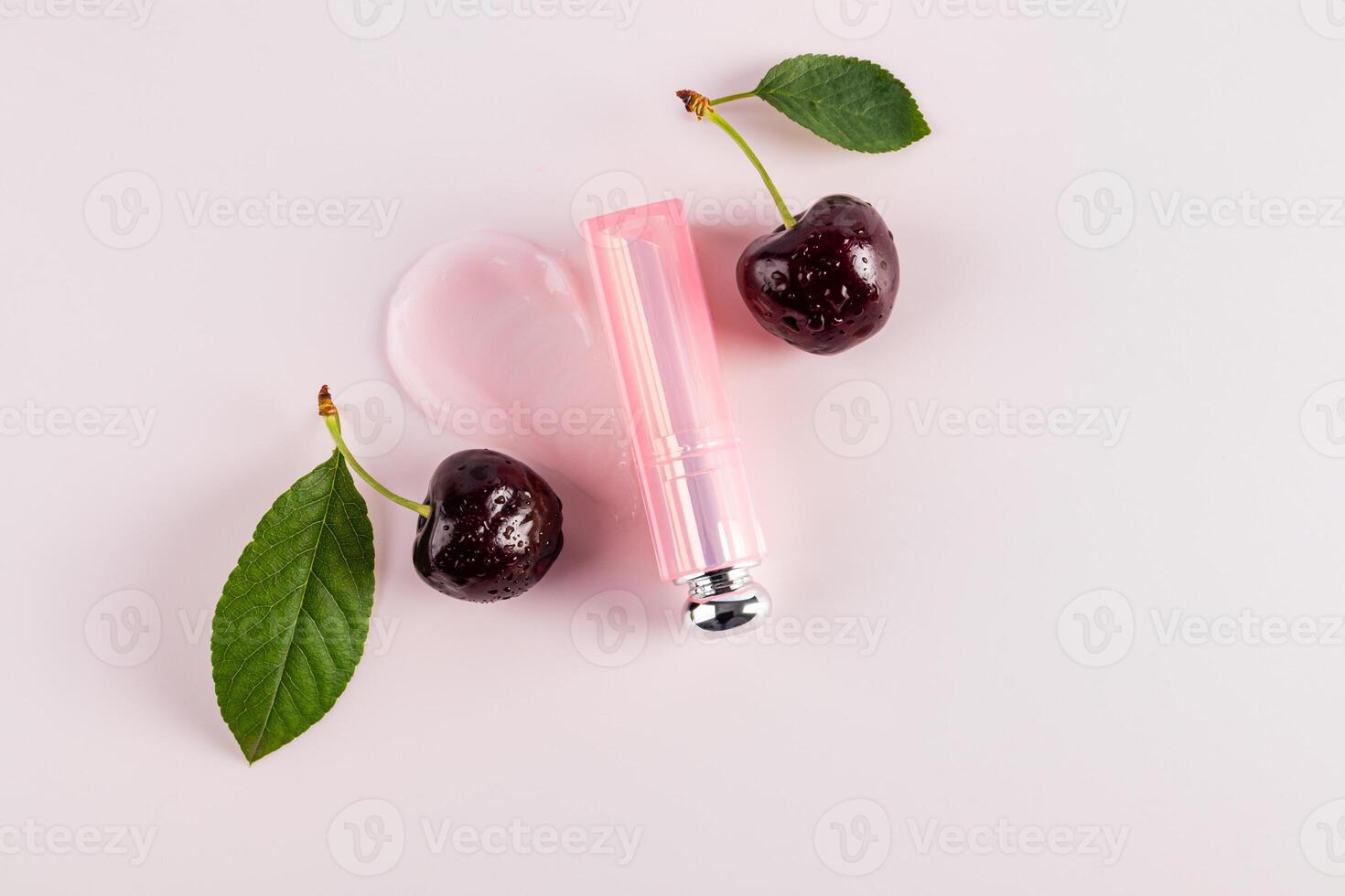 A beautiful package of lip balm or lipstick lies on sample of the texture of the product among ripe cherries. top view. A copy space. cosmetic layout photo