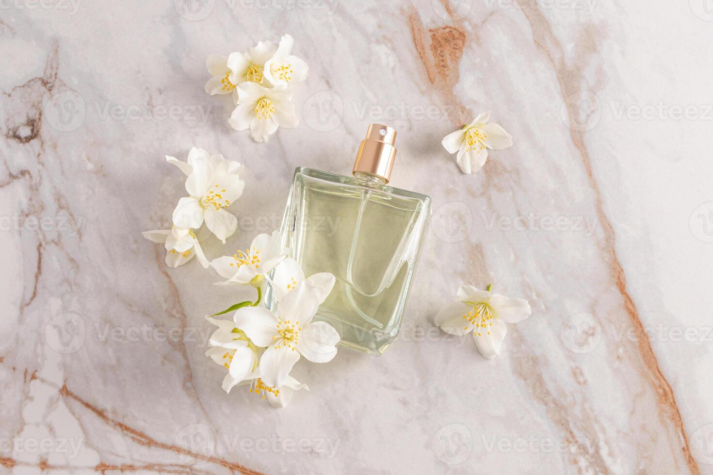 A glass transparent perfume bottle of lies on an abstract marble background with white jasmine flowers. top view. A blank bottle mockup. A copy space photo