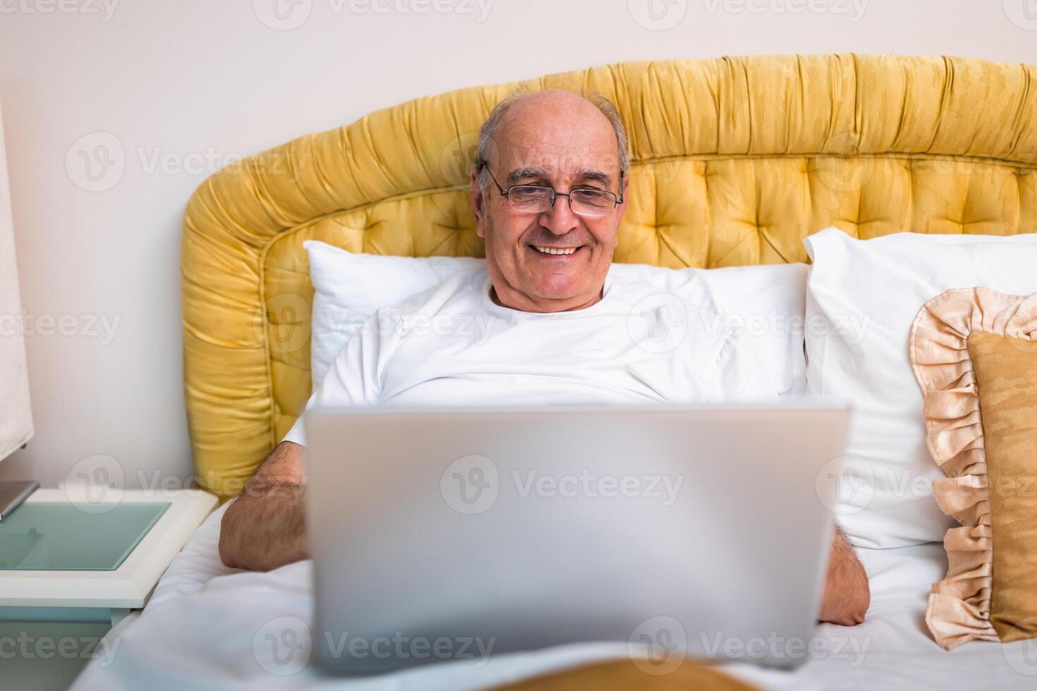 Senior male freelancer waking up and starting the day by checking emails and searching the internet on his laptop in bed. photo