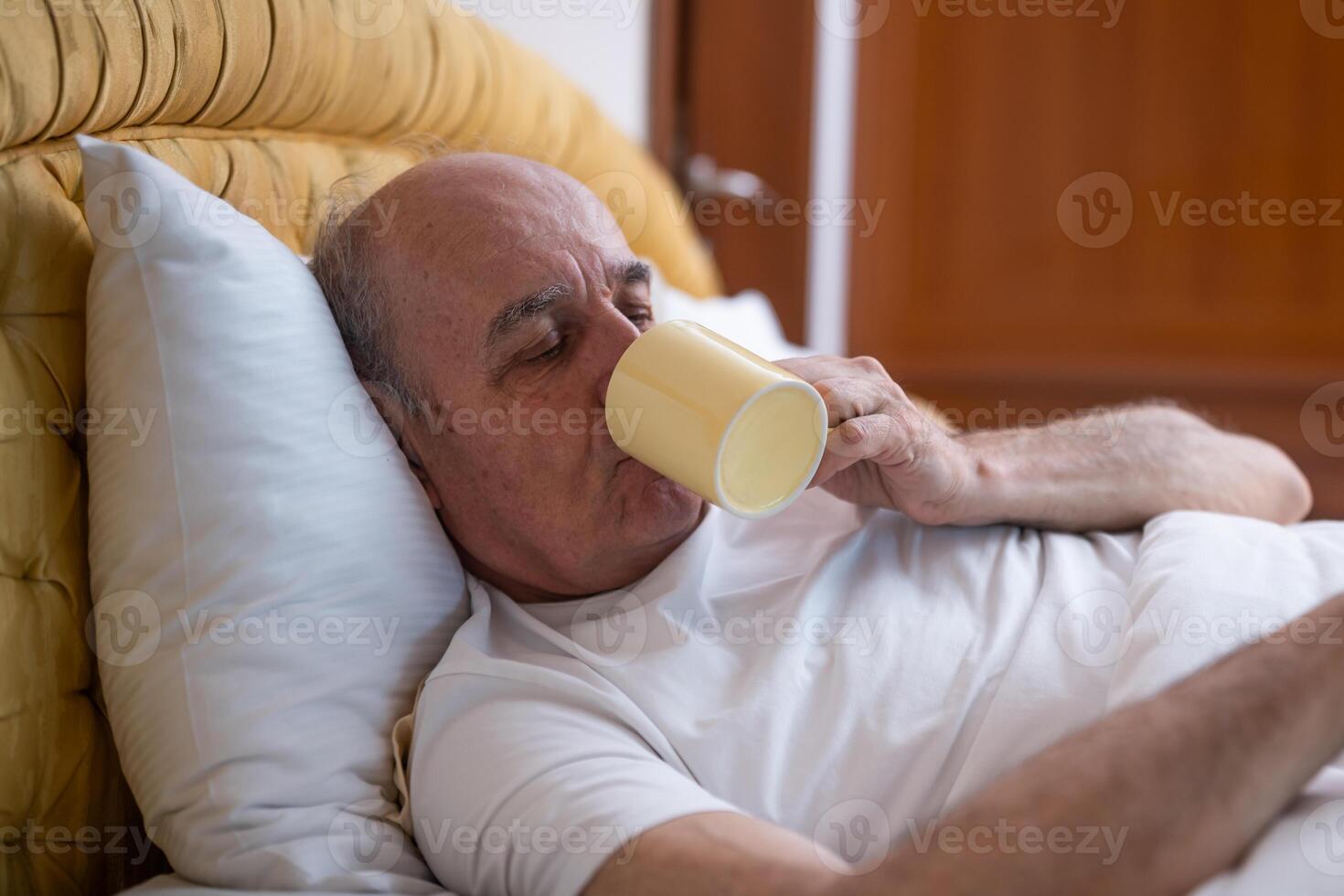 Senior male lying down, relaxed and refreshed, drinking coffee as the soft morning light fills the room. photo