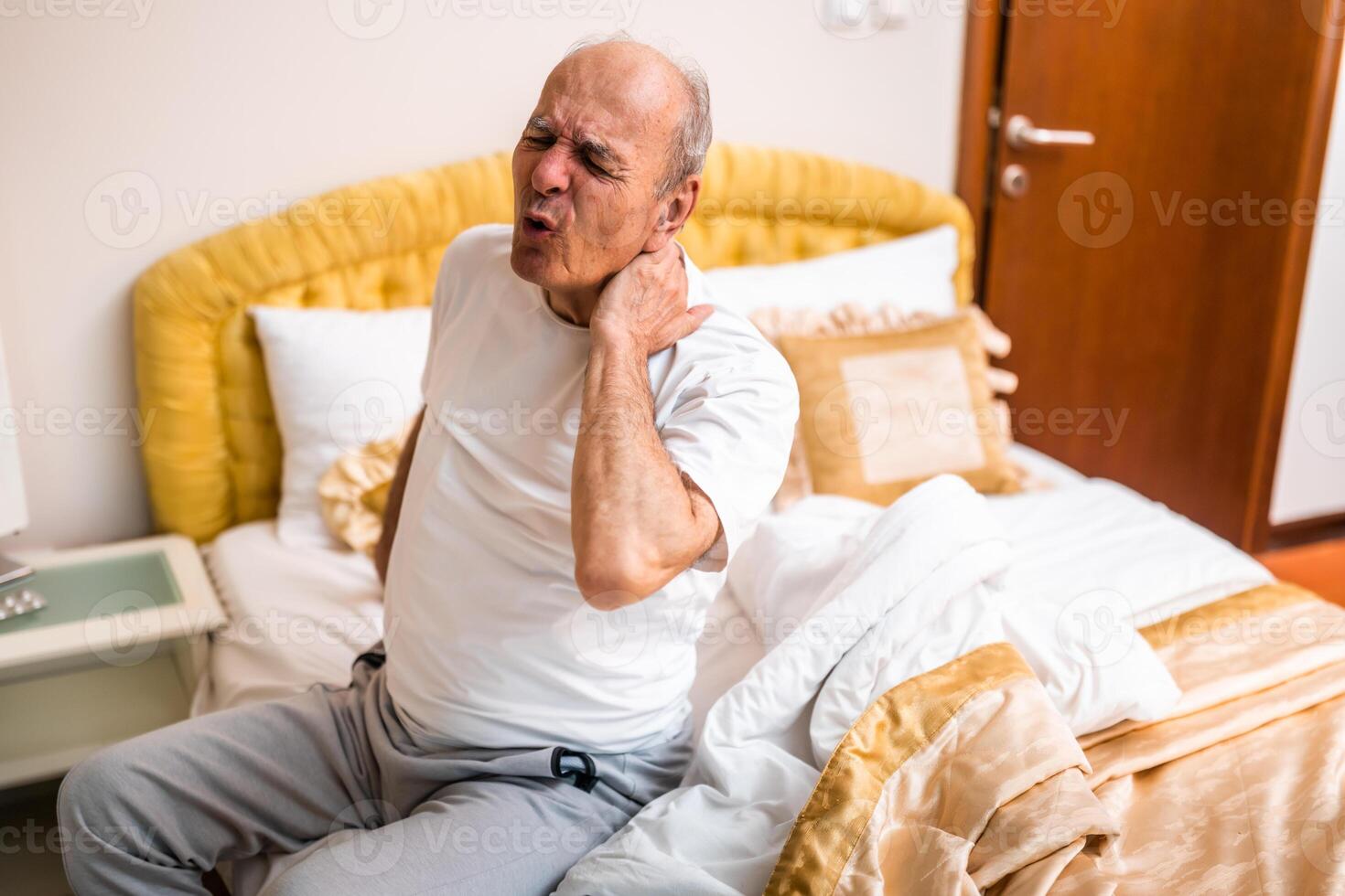 Aging man grimacing and shouting in pain due to a neck injury or sprain at dawn. photo