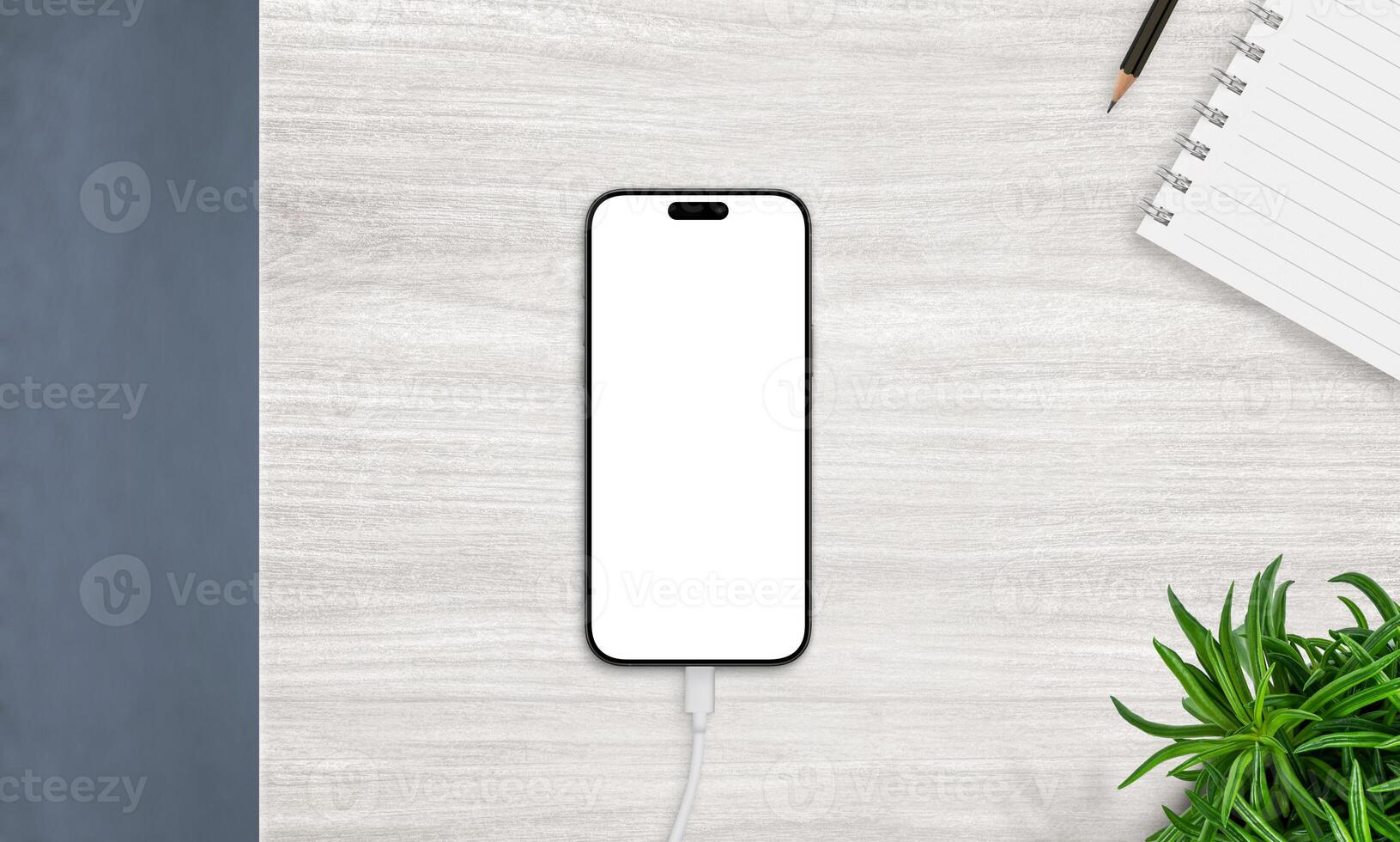 Top view of smartphone on charger with blank screen, placed on desk with notebook and plant. Ideal for productivity and app mockups photo