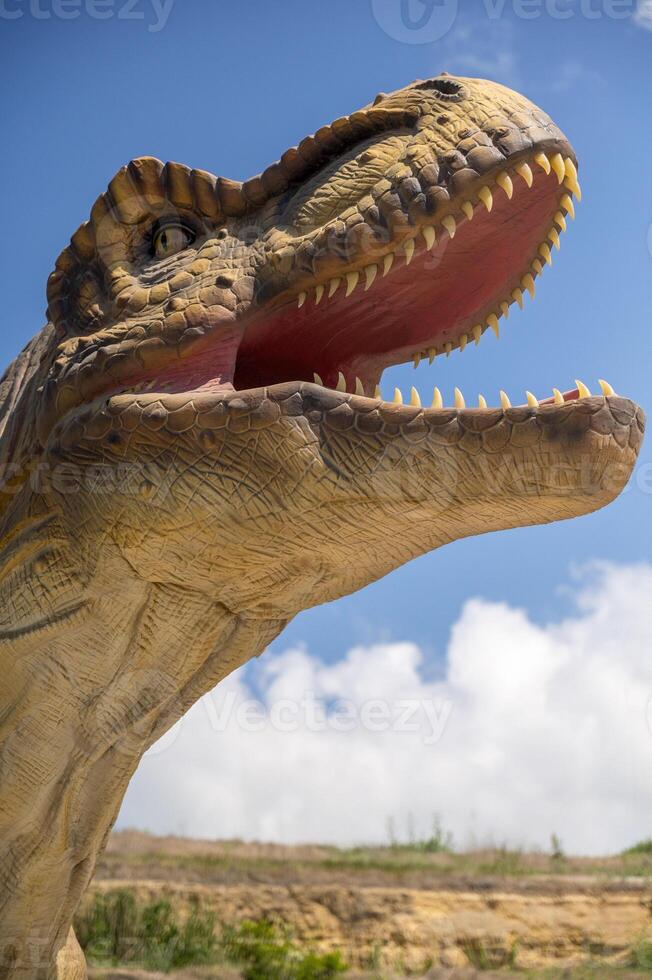 Artificial dinosaur tyrannosaurus, close-up of dinosaur head against sky background. With copy space. Jurassic Park with huge figure of predatory tyrannosaurus. You can see dinosaur teeth. vertical photo
