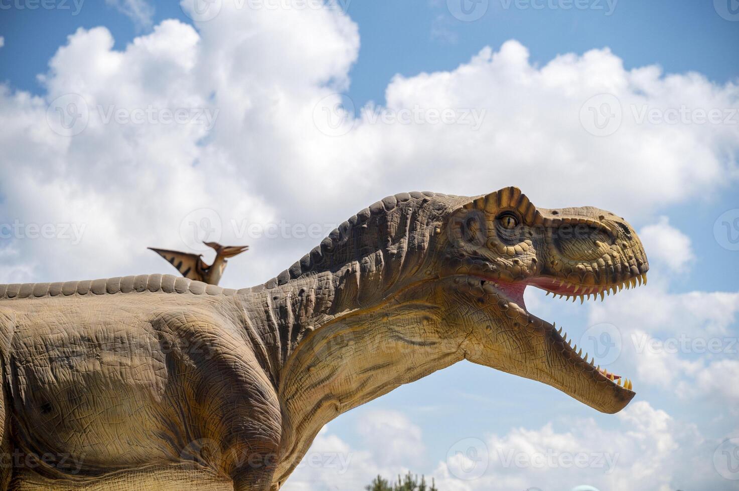 Artificial dinosaur tyrannosaurus, close-up of dinosaur head against sky background.Two dinosaurs. Pterodactyl and tyrannosaurus. One huge dinosaur and the other smaller. Photo in a cold shade