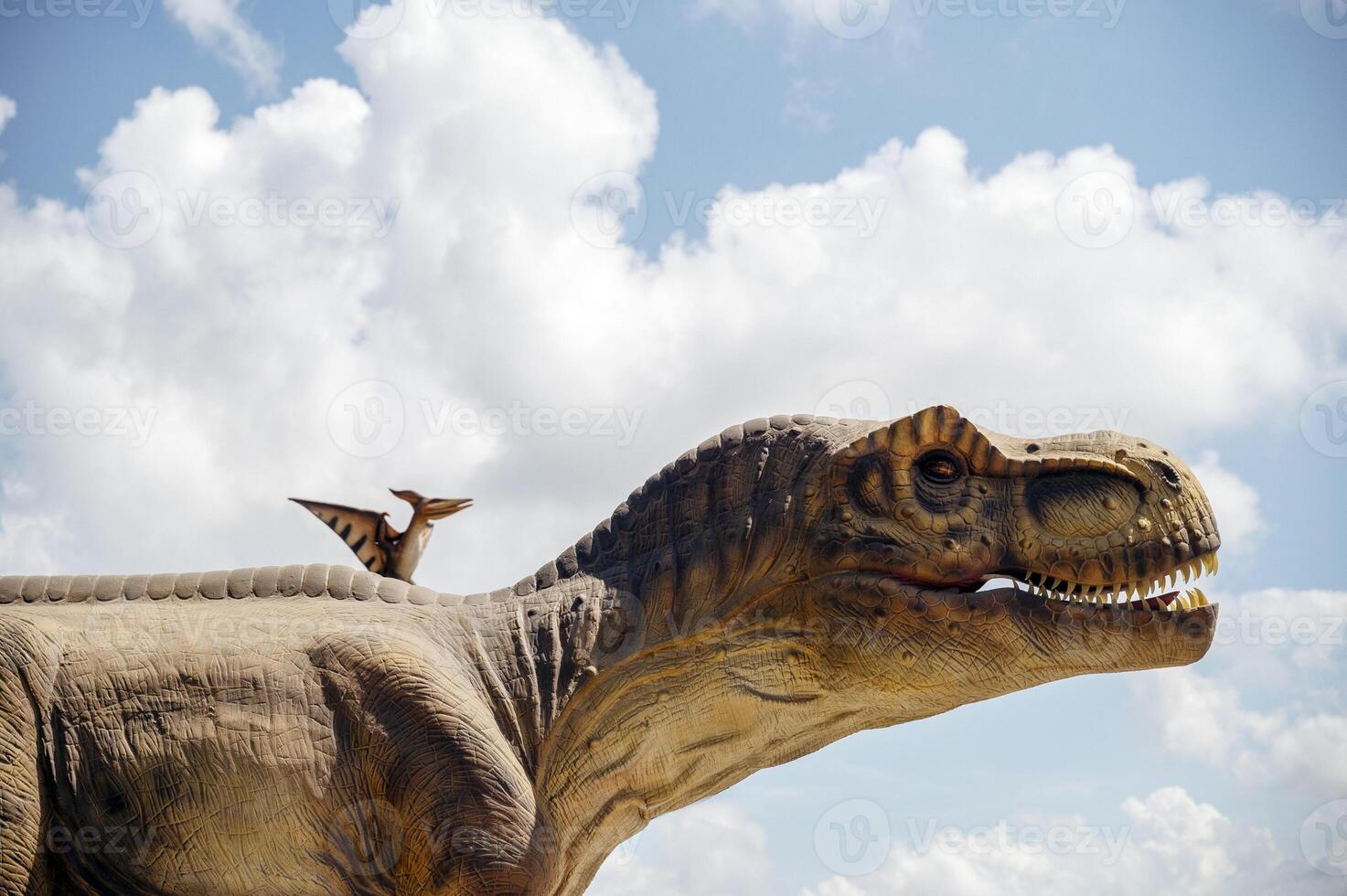 Artificial dinosaur tyrannosaurus, close-up of dinosaur head against sky background.Two dinosaurs. Pterodactyl and tyrannosaurus. One huge dinosaur and the other smaller. photo