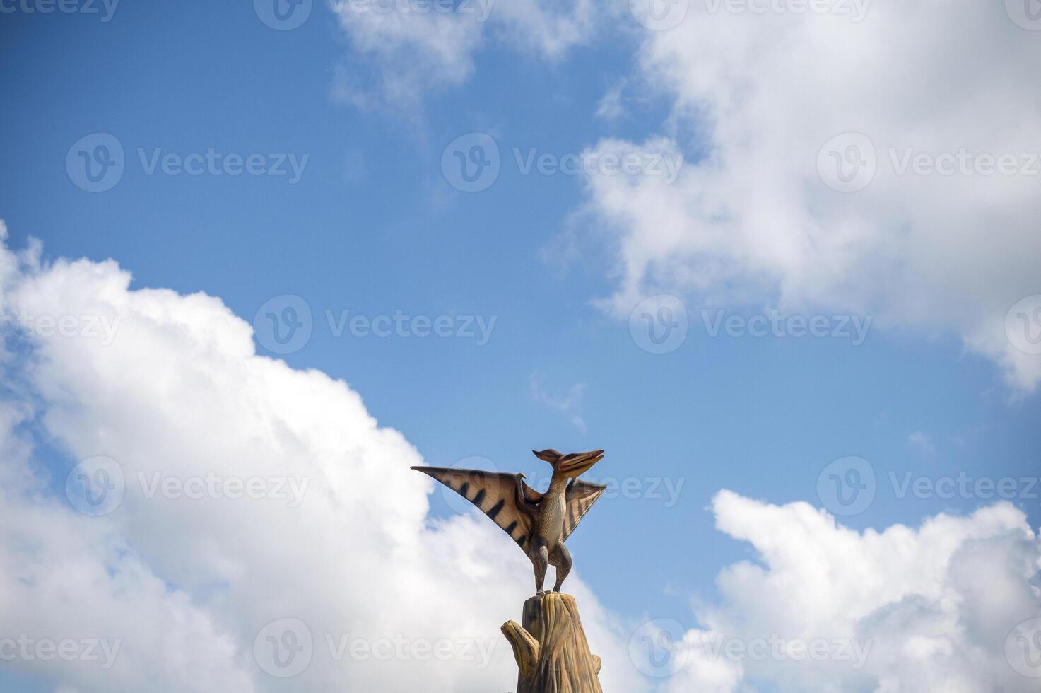 Pterodactyl against the sky. A single dinosaur statue sits on a tree trunk against the backdrop of clouds. copy space. horizontal photo. Clouds in a blue cloudy sky. High quality photo