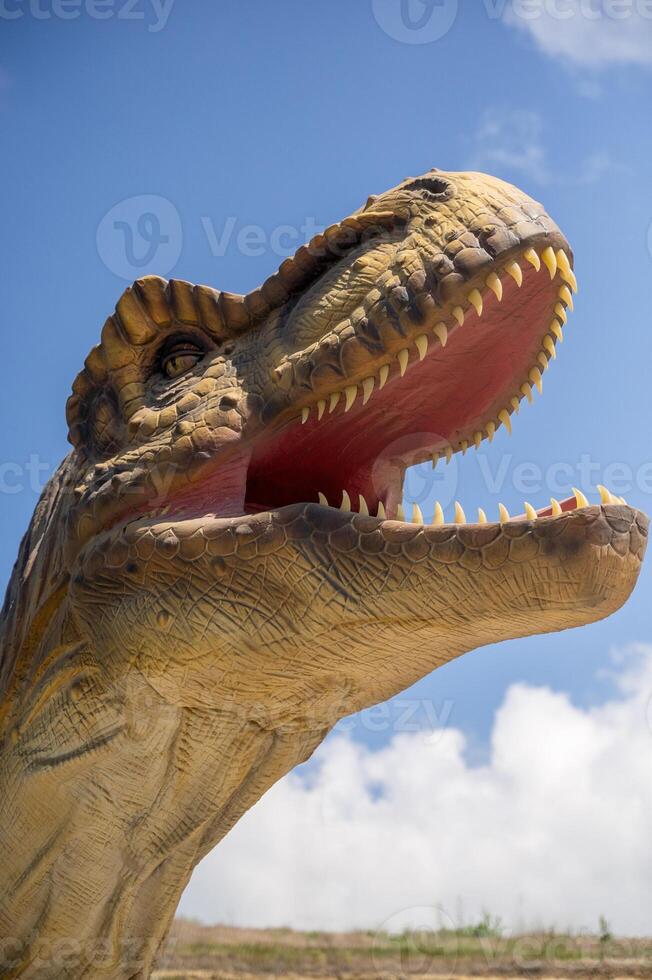 Artificial dinosaur tyrannosaurus, close-up of dinosaur head against sky background. With copy space. Jurassic Park with huge figure of predatory tyrannosaurus. You can see dinosaur teeth photo