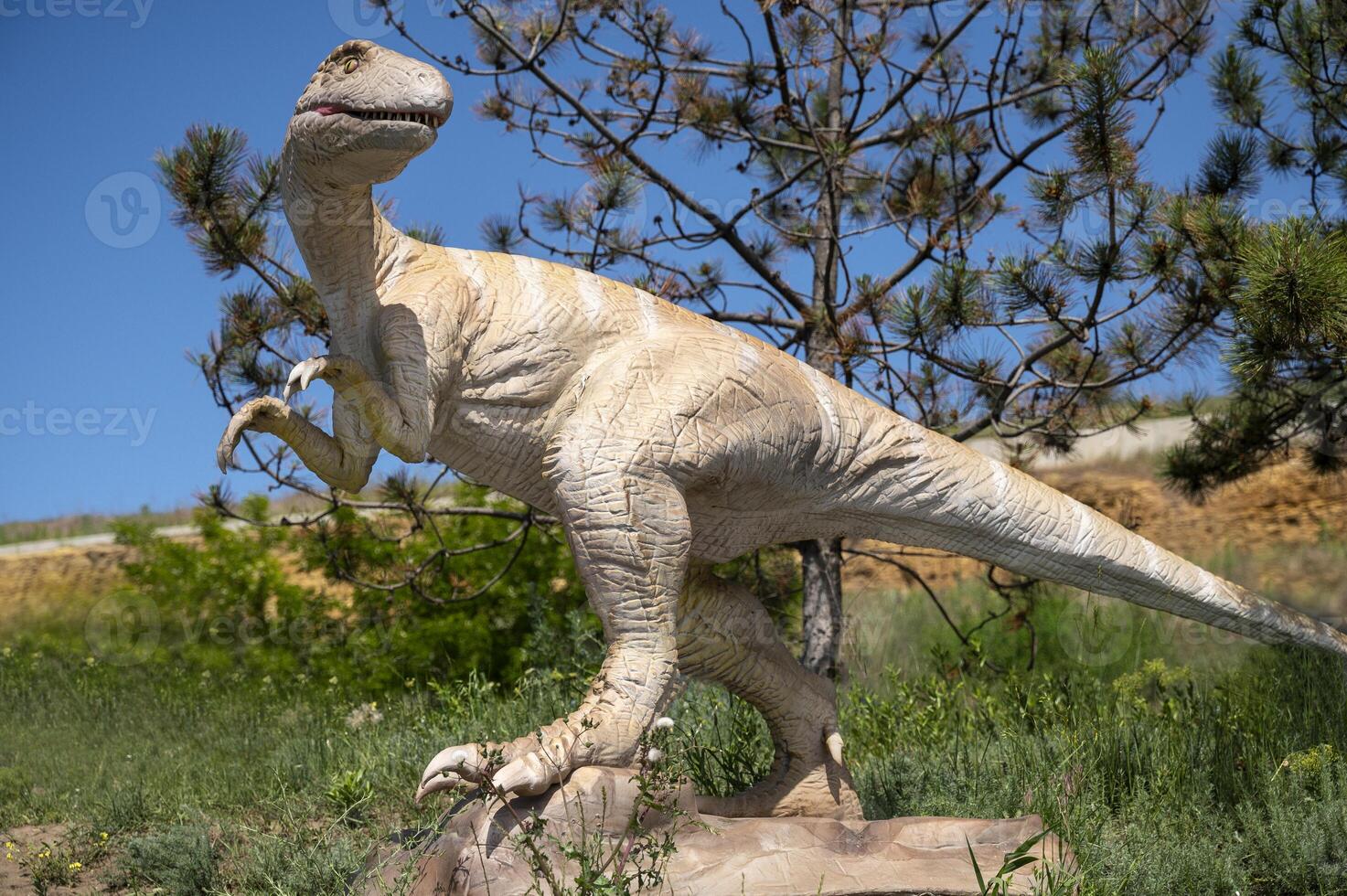 Dinosaur statue with a long tail. Dinosaur figure among trees in nature in the park. Against the background of blue sky and trees. copy space. photo
