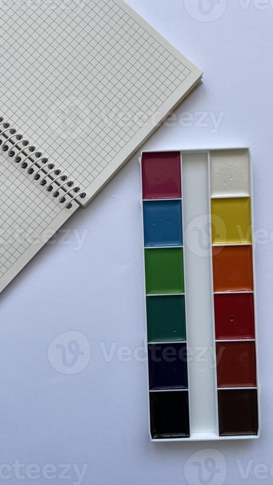 Top View of Watercolor Paint Set and Spiral Notebook on White Background. Back to School Creative Concept. Stationery for Drawing and Education. photo