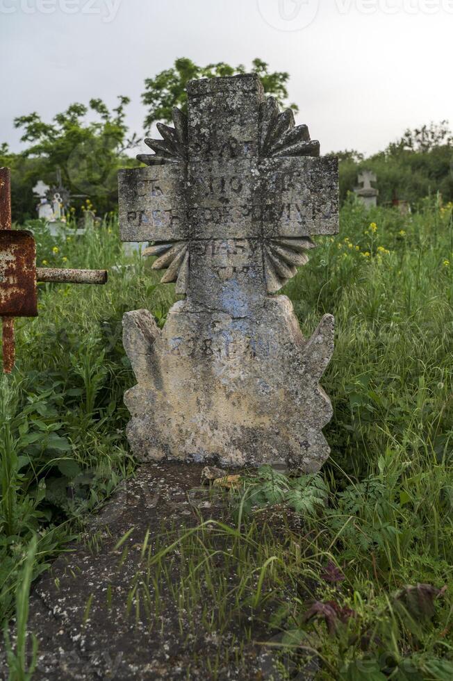 Stone cross in an old cemetery with a faded inscription. Old stone cross with inscriptions between the grass on a green field. Ancient history, travel. photo