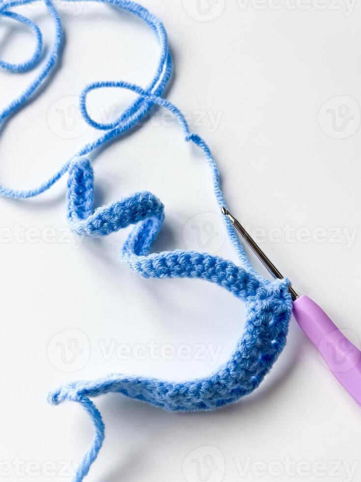 Blue crochet stitch with purple hook on white background photo
