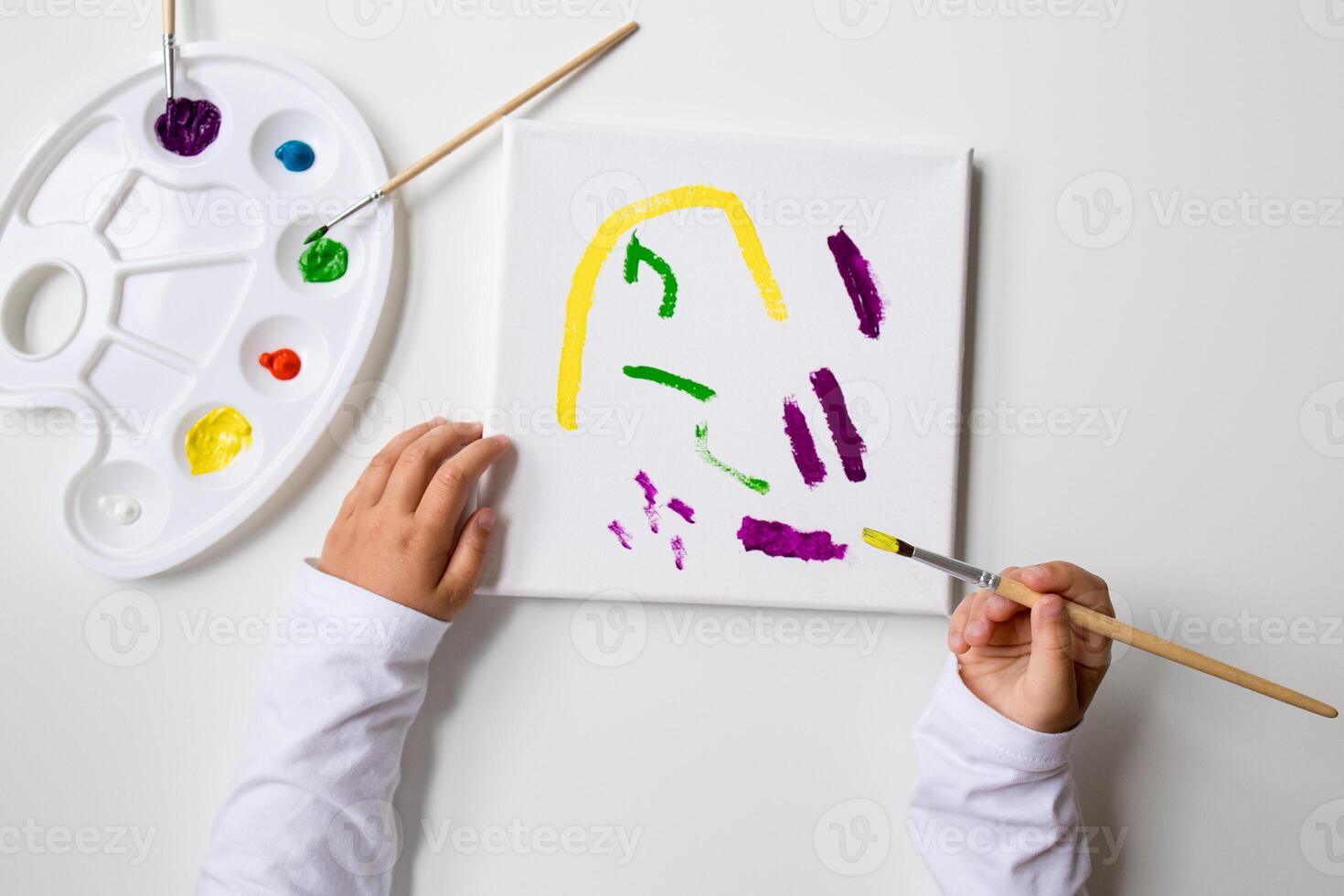 Child painting abstract art on canvas with color palette and brushes photo