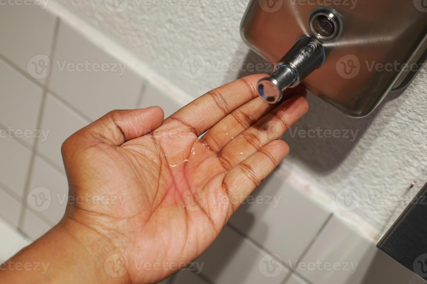 Hand Under Liquid Soap Dispenser in Clean Restroom Setting photo