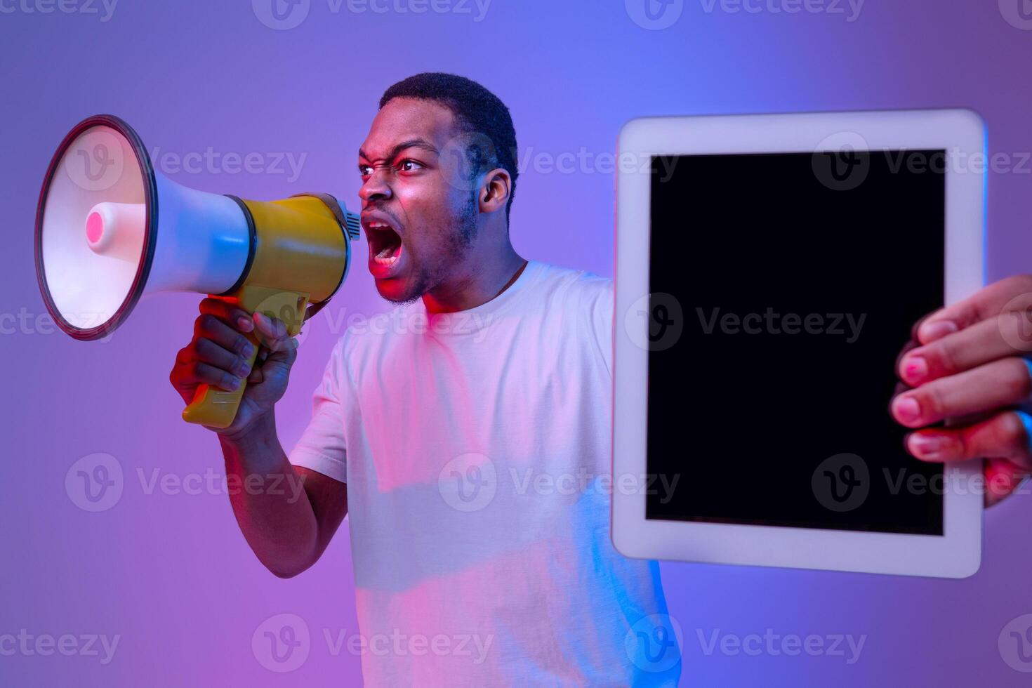 Emotional Black Guy Holding Digital Tablet With Blank Screen And Shouting To Loudspeaker, Making Announcement About New Website Or App, Standing In Vivid Neon Light Over Purple Background, Mockup photo