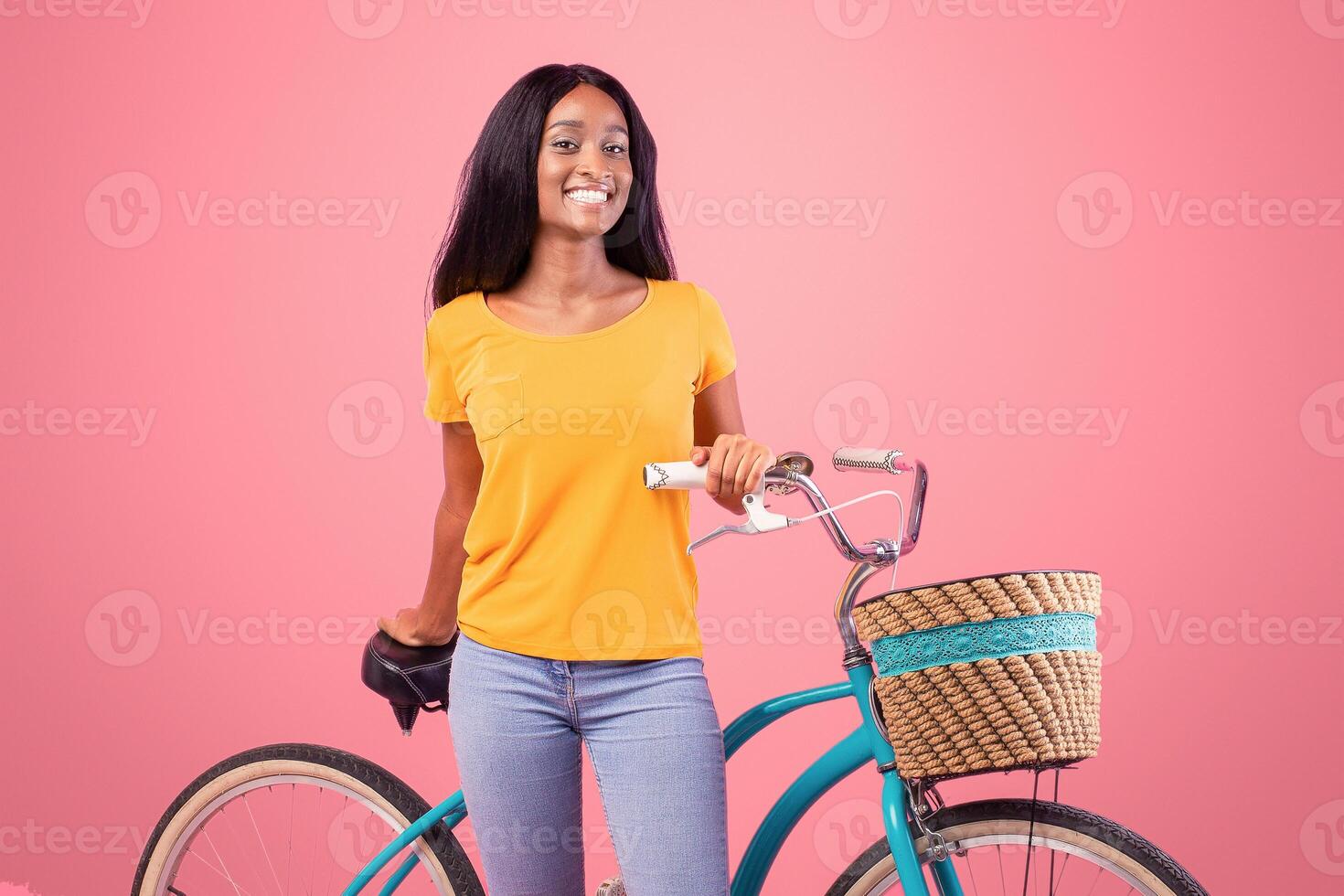 Full length portraif of pretty black lady with vintage bicycle smiling at camera on pink studio background. Positive African American woman going cycling, loving adventure and active sports photo
