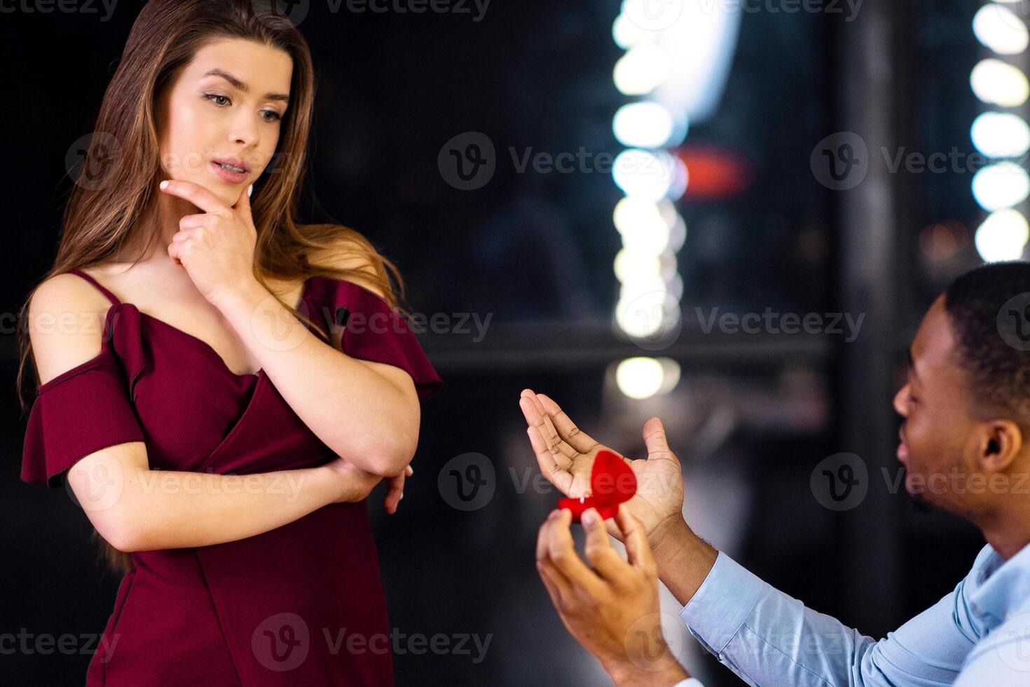 Black Man Begging Girlfriend To Marry Him, Making Marriage Proposal In Restaurant. Young Woman Hesitating With Answer, Having Doubts To Say Yes Or No, Standing With Thoughtful Face Expression photo